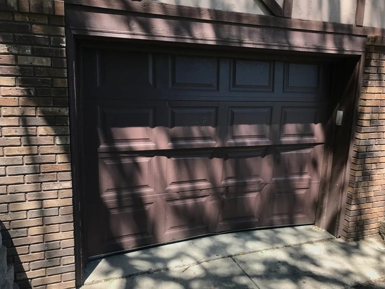 Black modern garage door with horizontal panels on brick wall with tree shadows cast across it