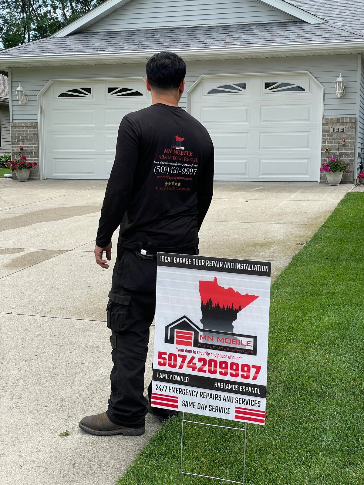 Garage door repair technician standing in driveway next to lawn sign advertising local mobile garage door repair and installation services